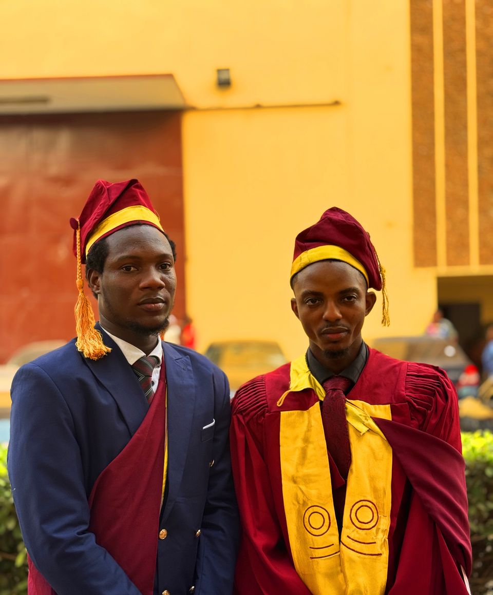 Two graduates in cap and gown attire standing proudly outdoors