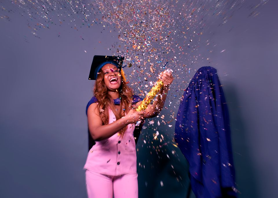 A laughing woman in a graduation cap firing a confetti cannon