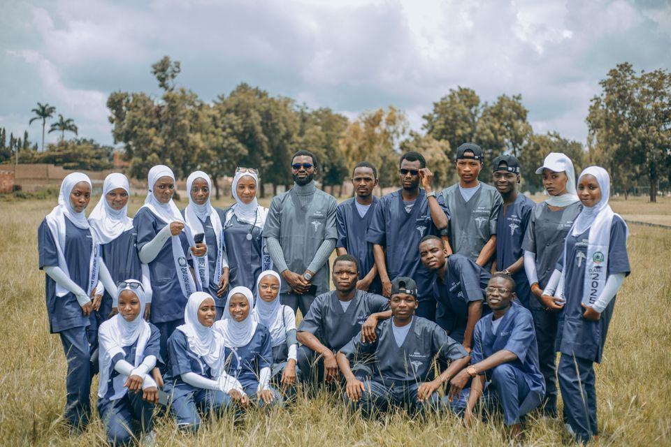 A cohort of medical students in scrubs posing together on a grassy field