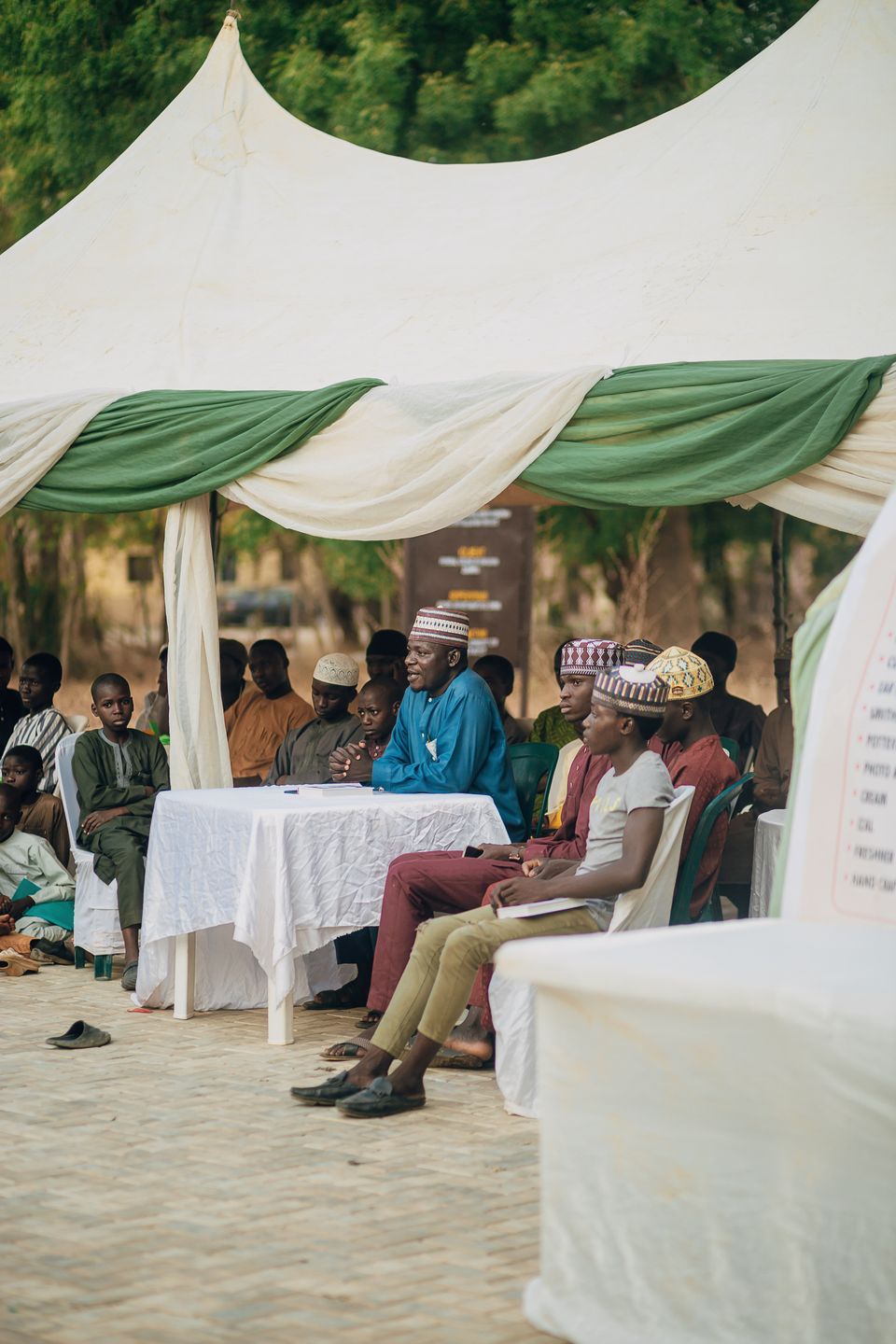 An outdoor community event under a green and white canopy with a high table