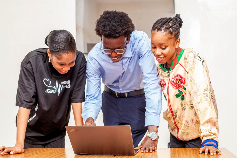 Three young students collaborating over a laptop, smiling