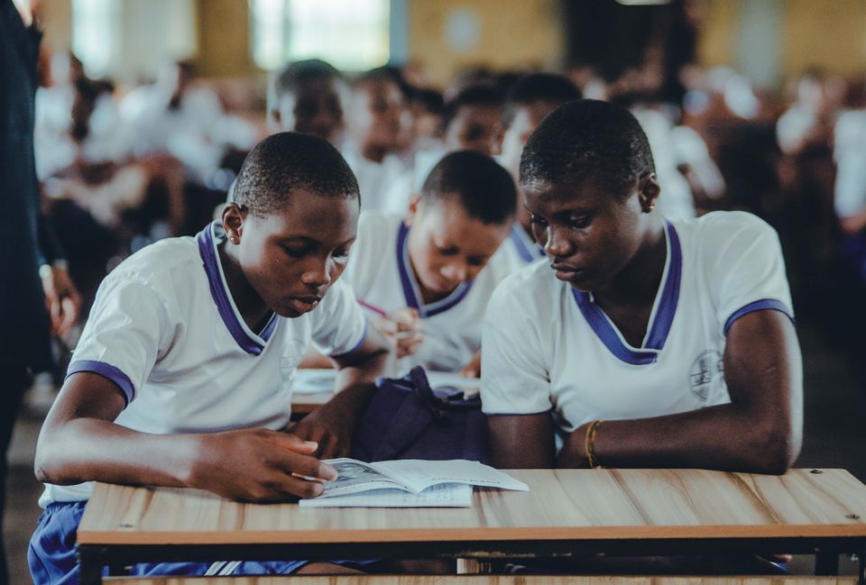 Two Nigerian students studying together from one textbook at a wooden desk