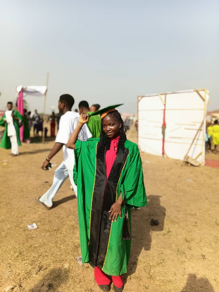 Nwaeze Lucy Ozioma smiling in her green academic gown at an outdoor university ceremony